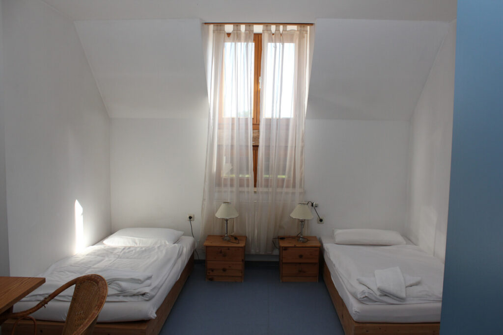 Ein Doppelzimmer, in dem zwei Betten stehen. Zwischen den Betten stehen Nachtkästchen.