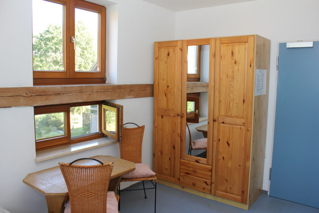 Ein Hotelzimmer mit einem großen Bauernschrank, einem Holztisch und zwei Stühlen